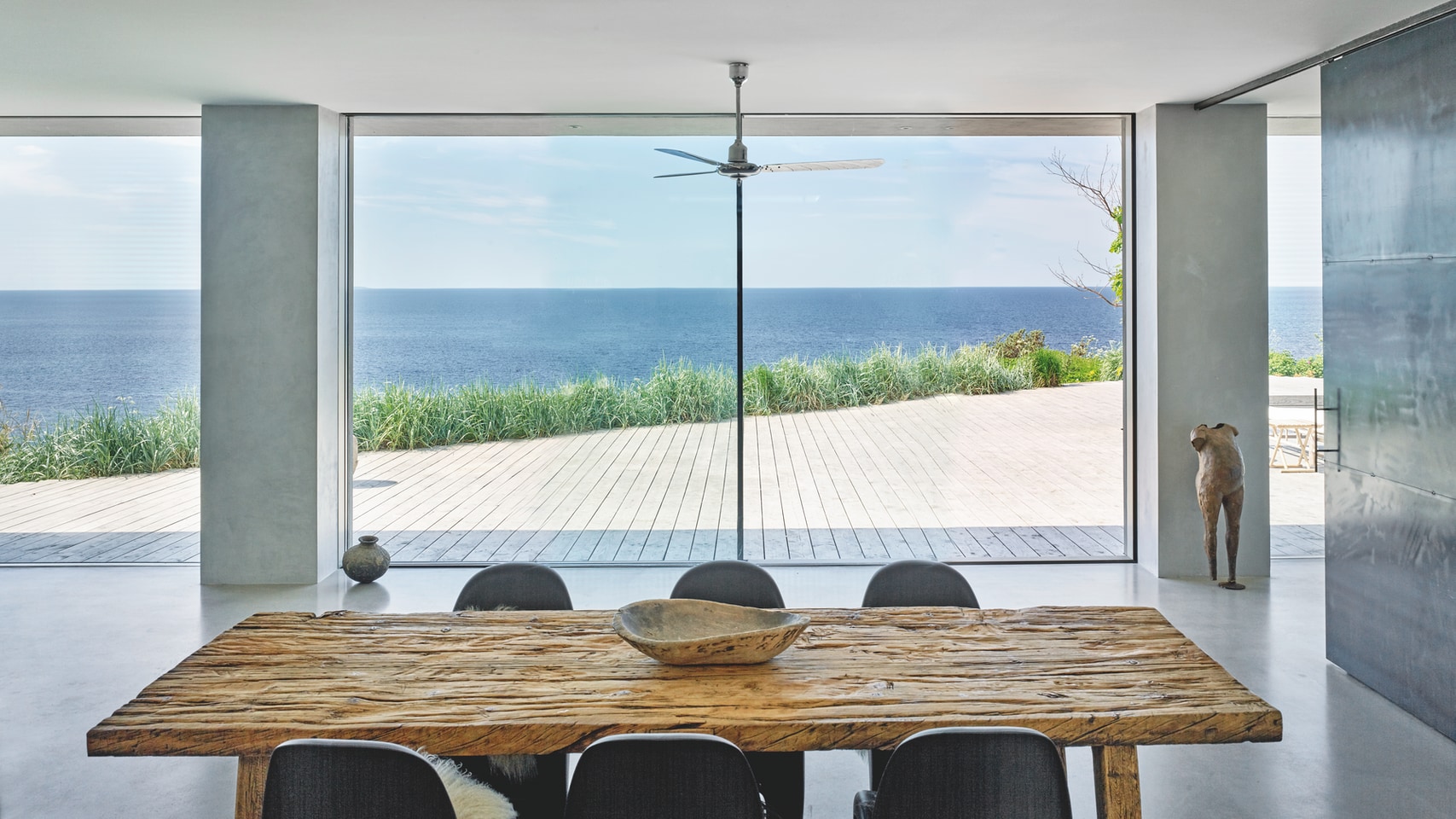 Utsikt mot hav gjennom store glassdører fra spiseplass