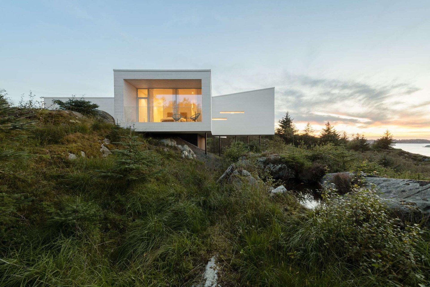Villa Austevoll plassert i terrenget på påler i ettermiddagslys