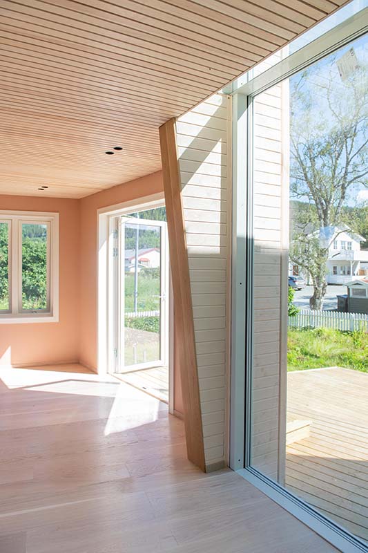 Detalj av første etasje med åpen terrassedør i det nye tilbygget, sett fra gangen med stor glassfasade.