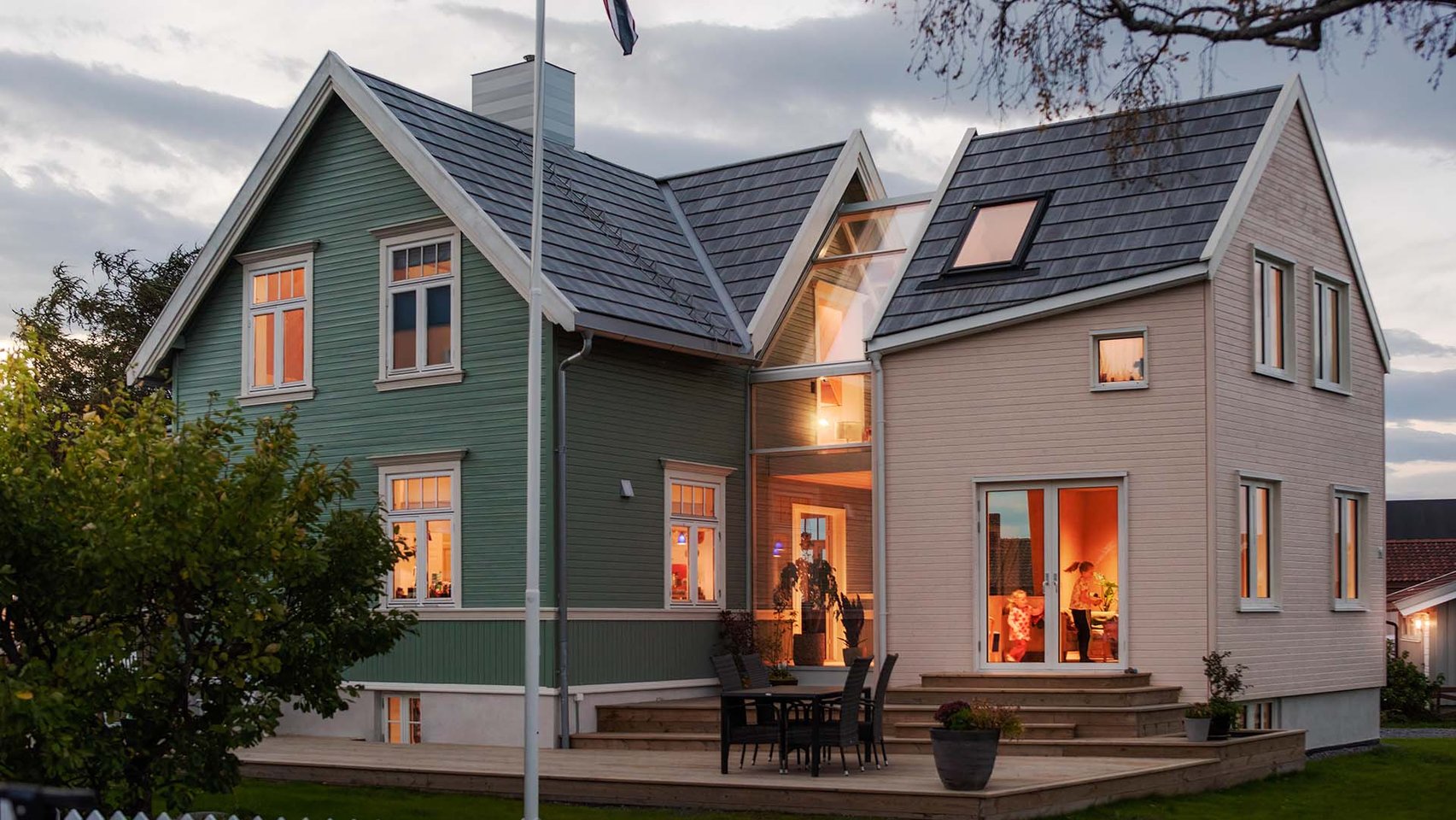 Enebolig i Trondheim, med det nye tilbygget i glass og tre på gavlveggen, sett i skumringen med varmt lys innenfra.